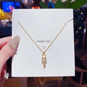 Close-up of gold lock pendant necklace with pavé zircons on a Thank You display card