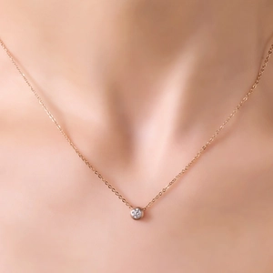 Minimalist 18K rose gold necklace with round solitaire pendant worn on collarbone
