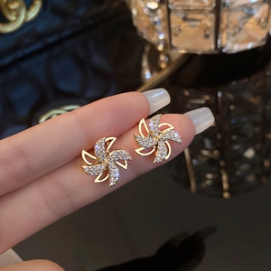 Luxury gold windmill earrings with shimmering pavé zircon crystals shown on fingers