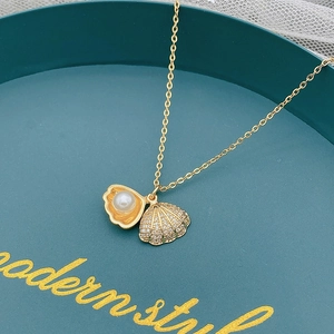 Dettaglio macro di una collana con ciondolo a conchiglia dorata con zirconi e perla bianca