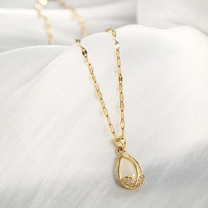 Close-up of golden tulip necklace with white opal teardrop pendant on silk background