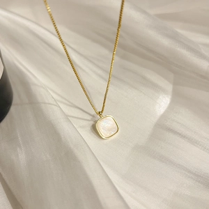 Elegant gold titanium necklace with a square shell pendant on soft white silk fabric