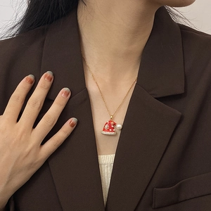 Gouden kerstmuts ketting met rood email en parel gedragen door elegant model