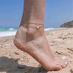 Gold double-layered anklet with a heart pendant engraved with letter A on beach