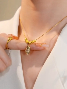 Detail of gold necklace with diamond leaf pendant and beads worn with white suit