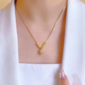 Detail of a textured golden sphere pendant with matte beads on a delicate chain