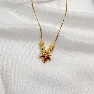 Macro view of golden maple leaf pendant with red gemstones and six matte beads