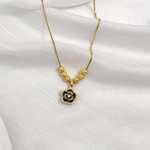 Detail view of gold necklace featuring black floral pendant and frosted beads on a box chain