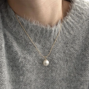 Elegante goldene Halskette mit weißer Perle auf einem grauen Strickpullover präsentiert