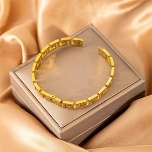 Goldener Manschettenarmreif aus Titanstahl mit hohlem griechischem Muster auf Seidenhintergrund