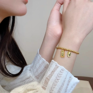 Detail of gold beaded bracelet featuring a gold bar pendant and lucky charm on wrist