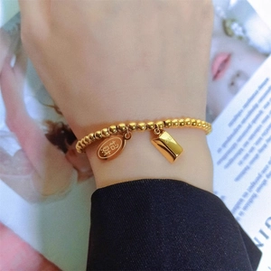 Gold beaded elastic bracelet with lucky charm pendants and miniature gold bar