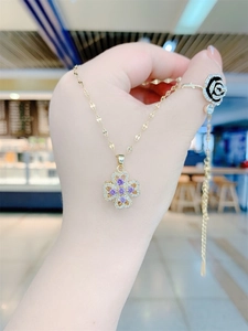 Detailed view of rotating gold necklace with purple clover pendant and black rose ring