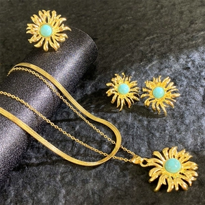 18K gold plated titanium sunburst jewelry set with turquoise stone on dark surface