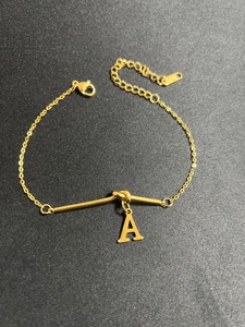 Detail eines vergoldeten Titanstahl-Knotenarmbands mit A-Anhänger und Karabinerverschluss