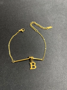Nahaufnahme eines goldenen Titanarmbands mit Anhänger Buchstabe B auf Texturhintergrund