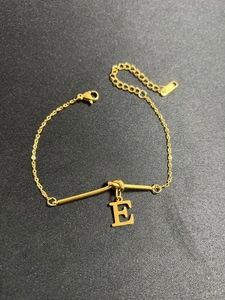 Detailansicht eines goldenen Kettenarmbands mit fettem E-Anhänger und Karabinerverschluss
