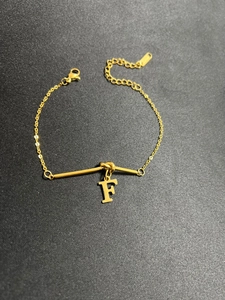 Detail eines goldenen Titanstahlarmbands mit F-Anhänger und praktischem Karabinerverschluss