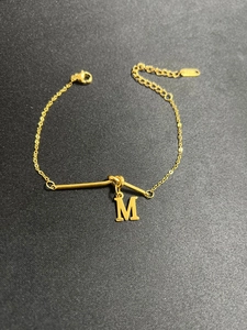 Makroaufnahme: Vergoldetes Edelstahl-Armband mit Buchstabe M und Stab-Anhängern