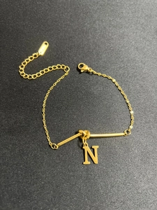 Detail eines verstellbaren goldfarbenen Armbands mit N-Anhänger, Karabiner und Verlängerung