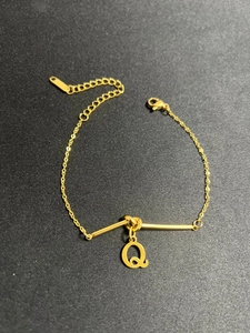 Detail eines goldenen Edelstahlarmbands mit Knoten-Design und Buchstabe-Q-Anhänger