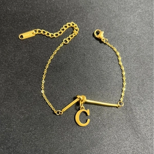Goldenes Armband aus Titanstahl mit C-Buchstabenanhänger auf strukturiertem Hintergrund