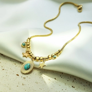 Goldene Schlangenkette mit Türkis-Steinen und Stern-Anhängern auf Seidenstoff