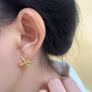 Close-up of a gold-toned starfish earring featuring a textured surface on a model's ear