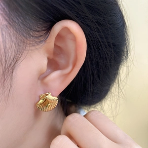 Macro shot of gold shell earrings on ear showing delicate vertical textures and metallic luster
