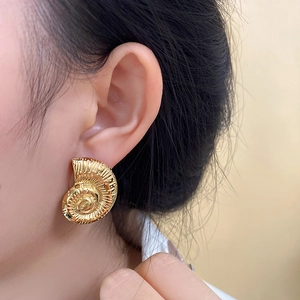 Close-up of golden nautilus shell earrings featuring vintage spiral textures on a model