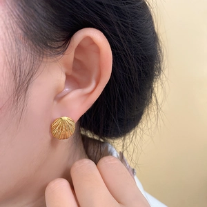 Detail of a gold seashell earring with radial stripes worn by a model on a soft background