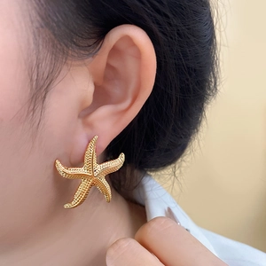 Close-up of golden starfish stud earring featuring detailed relief texture on earlobe