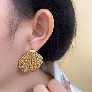 Macro shot of large golden seashell earrings showing fine radial textures on a model