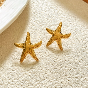 Macro shot of gold starfish earrings with textured hammered finish on white surface