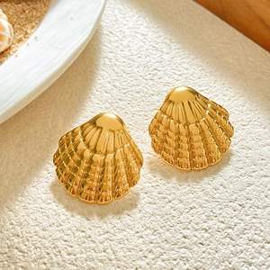 Macro shot of gold shell earrings with radial textures on a textured white surface