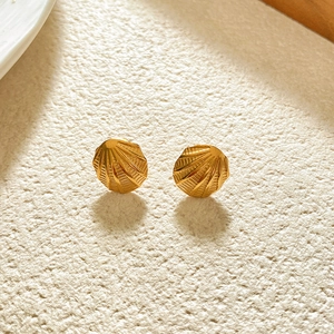 Macro detail of gold-plated conch shell earrings with radiant texture on beige stone