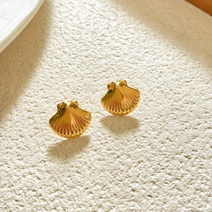Close-up of golden shell stud earrings with textured ridges and polished metallic finish