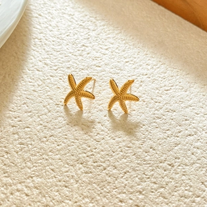 Macro detail of gold starfish earrings with textured surface on a minimalist background