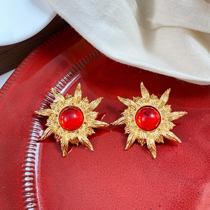 Detail of vintage sun-shaped gold earrings with large red round resin stone centers