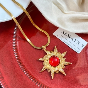 Macro detail of sunburst pendant with red gemstone on golden snake chain necklace