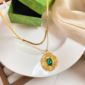Macro detail of gold layered necklace with green gemstone pendant on silk