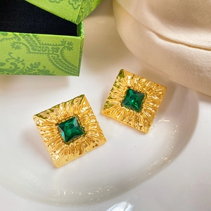 Macro shot of vintage gold square stud earrings with green center stone on silk