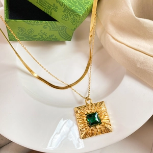 Detail of double-layered gold necklace with square green zircon pendant on white tray