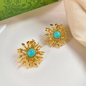 Macro shot of gold sunburst earrings with turquoise stones on a green floral gift box