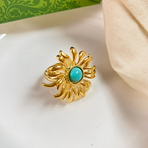 Detailed close-up of a golden flower ring set with a round turquoise stone on soft fabric
