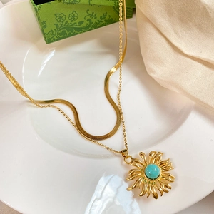 Detail of gold double-layer necklace with sunburst turquoise pendant on white ceramic plate