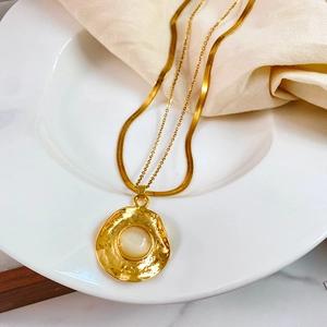 Close-up of gold layered snake chain and textured medallion with white opal-like stone