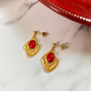 Close-up of vintage gold earrings with red textured stone on white marble surface