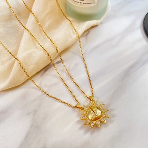 Détail du pendentif soleil doré avec gravure You are my Sunshine sur un fond en marbre blanc