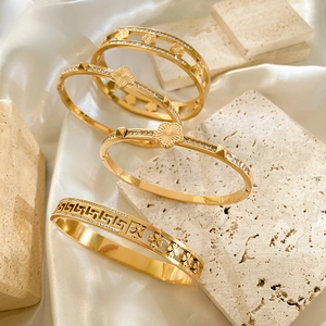Detail van vier gouden armbanden met klaver- en geometrische patronen op zijde